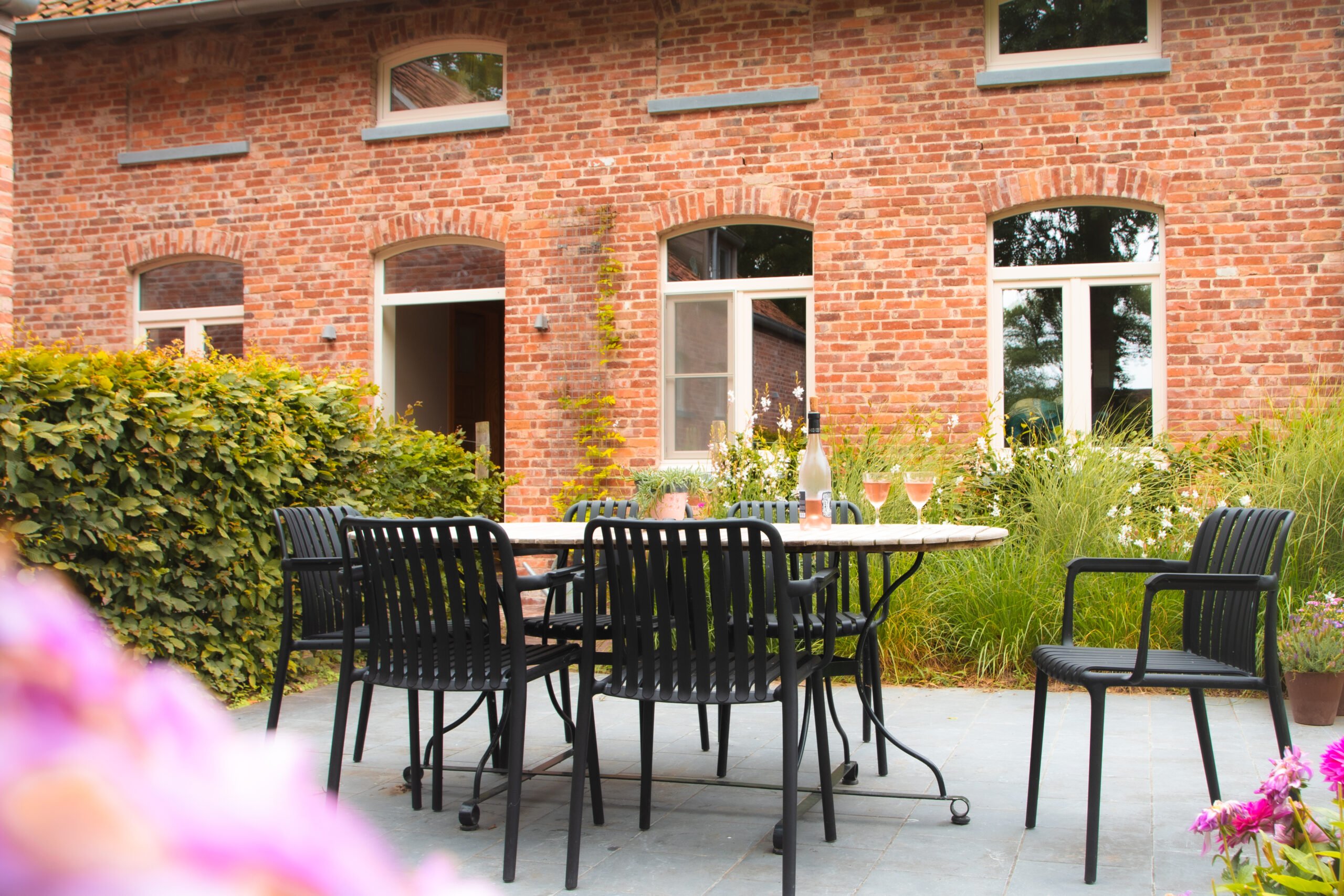 B&B bij Brugge Foto van een terrastafel met 2 gevulde wijnglazen bij de voorgevel van een landelijk huis